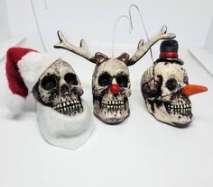 three skulls wearing santa hats and antlers on white surface with red nose ring in foreground