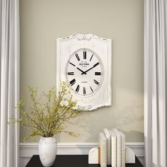 a white clock mounted to the side of a wall next to books and a vase