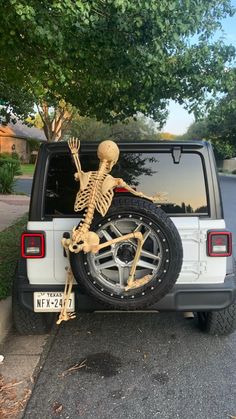 a skeleton sitting on the back of a white jeep parked in front of a tree