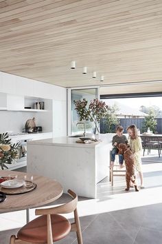 two people sitting at a kitchen table with a dog in front of them and an open door leading to the back yard