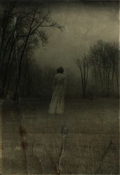 a woman standing in the middle of a field with trees behind her and foggy sky above