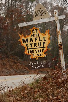 an old maple syrup sign is on the side of the road in front of some trees