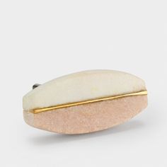 a white and gold brooch sitting on top of a white surface with a yellow stripe