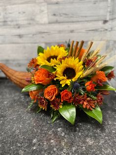 a bouquet of sunflowers and other flowers sits on a stone surface in front of a wooden wall