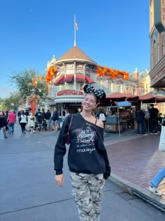 a woman standing in front of a building with mickey mouse ears on her head and other people walking around