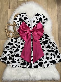 a black and white cow print dress with pink bow on the front, sitting on a wooden floor