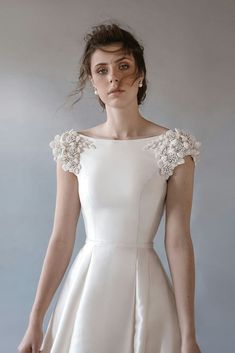 a woman wearing a white dress with flowers on the shoulders and shoulder, standing in front of