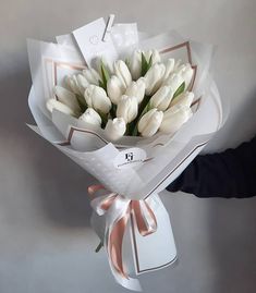 a bouquet of white tulips wrapped in paper and tied with a ribbon, held by someone's hand