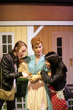 three women standing next to each other in front of a house