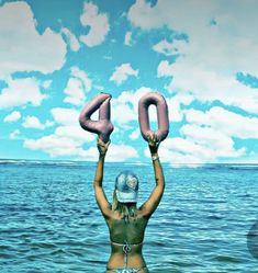 a woman standing in the water holding up two pink donuts that spell out 40