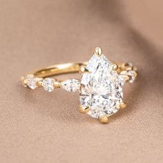 an oval cut diamond ring with pear shaped diamonds on the band and side stones in yellow gold