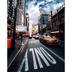 a city street filled with lots of traffic and tall buildings under a cloudy blue sky