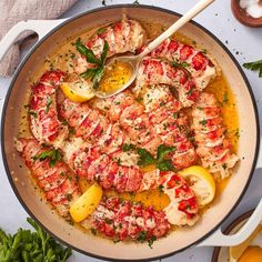 a pan filled with shrimp and lemons on top of a white table next to utensils