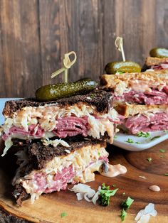 two sandwiches cut in half sitting on top of a cutting board next to pickles