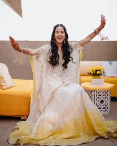 a woman sitting on top of a bed in a yellow and white dress with her arms outstretched