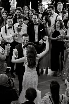 the bride and groom are dancing together at their wedding reception in front of a large group of people