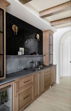 a kitchen with wooden cabinets and black marble counter tops, along with wine bottles on the shelves