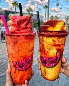 two people holding up drinks with strawberries and watermelon on the rims