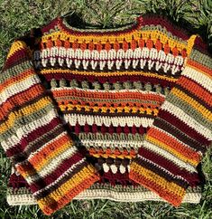 a multicolored crocheted sweater laying on the ground in the grass with it's sleeves open