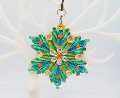 an ornament is hanging on a white tree with orange, blue and green leaves