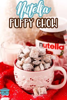 a cup filled with puppy chow sitting on top of a red cloth next to a bottle of nutella