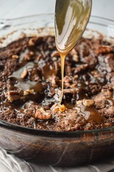 a spoon drizzling caramel sauce on top of a chocolate dessert in a glass dish