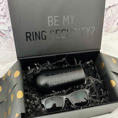 an open box containing sunglasses and a case with the words be my ring security?