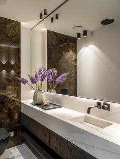 a vase with flowers in it sitting on a bathroom counter next to a sink and mirror