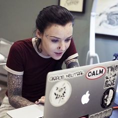 a woman sitting in front of a laptop computer with tattoos on her face and arm