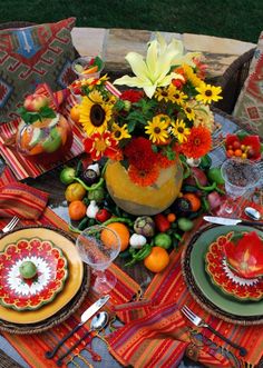 an outdoor table set for two with flowers and fruit on the placemat, napkins and plates