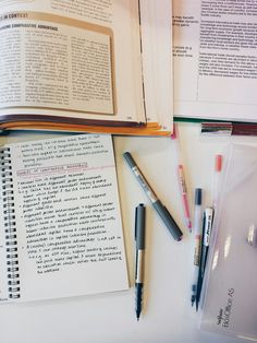 an open book and two pens on top of a table next to some books with writing utensils