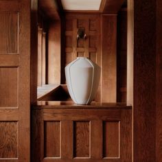 a large white vase sitting on top of a wooden shelf next to a door way