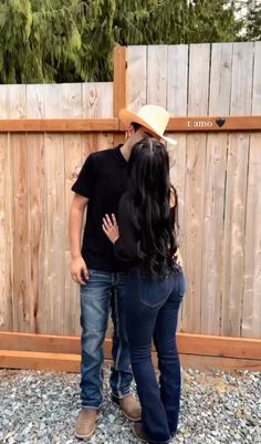 a man and woman kissing in front of a wooden fence