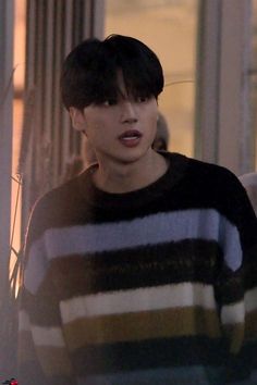 a young man with black hair wearing a striped sweater