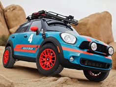 a blue car with red wheels and orange rims parked in the sand next to rocks