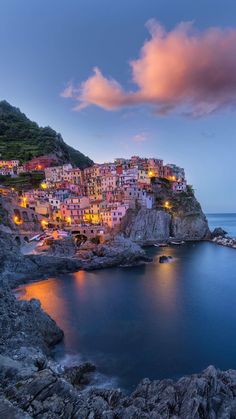 the village is lit up at night on top of a cliff overlooking the water and rocks