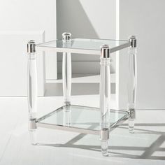 a clear glass table with two legs on the floor in front of a white wall