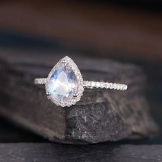 a pear shaped blue topazte and diamond ring sitting on a rock with its reflection in the water