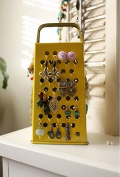 a yellow purse with lots of earrings hanging from it's sides on a white shelf