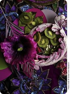 an arrangement of fruit and flowers on a purple table cloth with sequins in the background