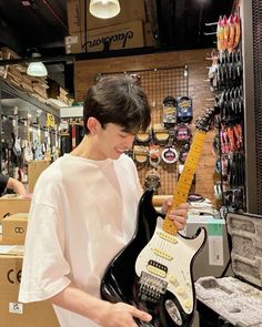 a young man is playing an electric guitar in a store with other items on the shelves