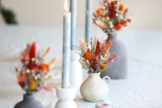 three vases with flowers in them on a table next to candles and other decorations