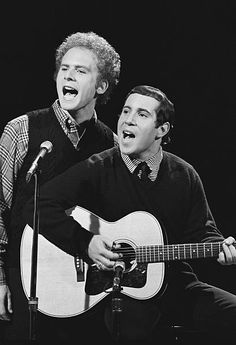 two men singing into microphones while holding guitars