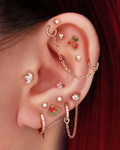 a woman with red hair wearing ear cuffs and piercings on her ears, all in different colors