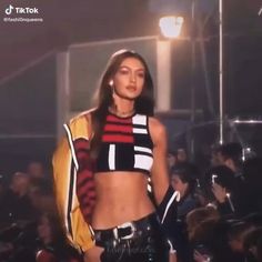 a woman is walking down the runway wearing leather pants and a cropped top with stripes on it