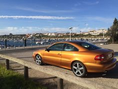 an orange car is parked on the side of the road near some water and boats