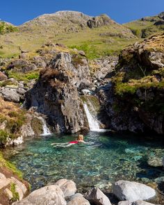 a person in a kayak near a waterfall and some rocks on the side of a hill