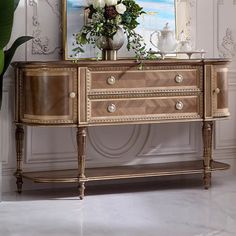 an ornate dresser with flowers and vases on it in front of a white wall