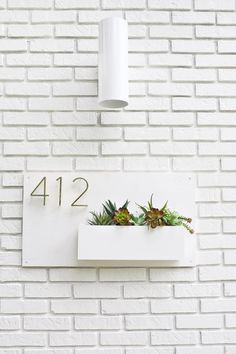 a white brick wall with a planter and numbers on the front, below it