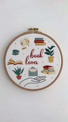 a hand embroidered book lover with books and plants on it's side, in front of a white wall